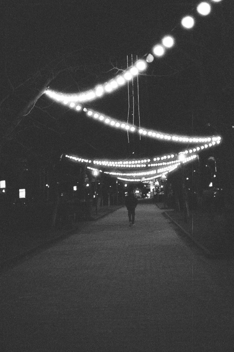 person walking down a dark street at night, under string lights