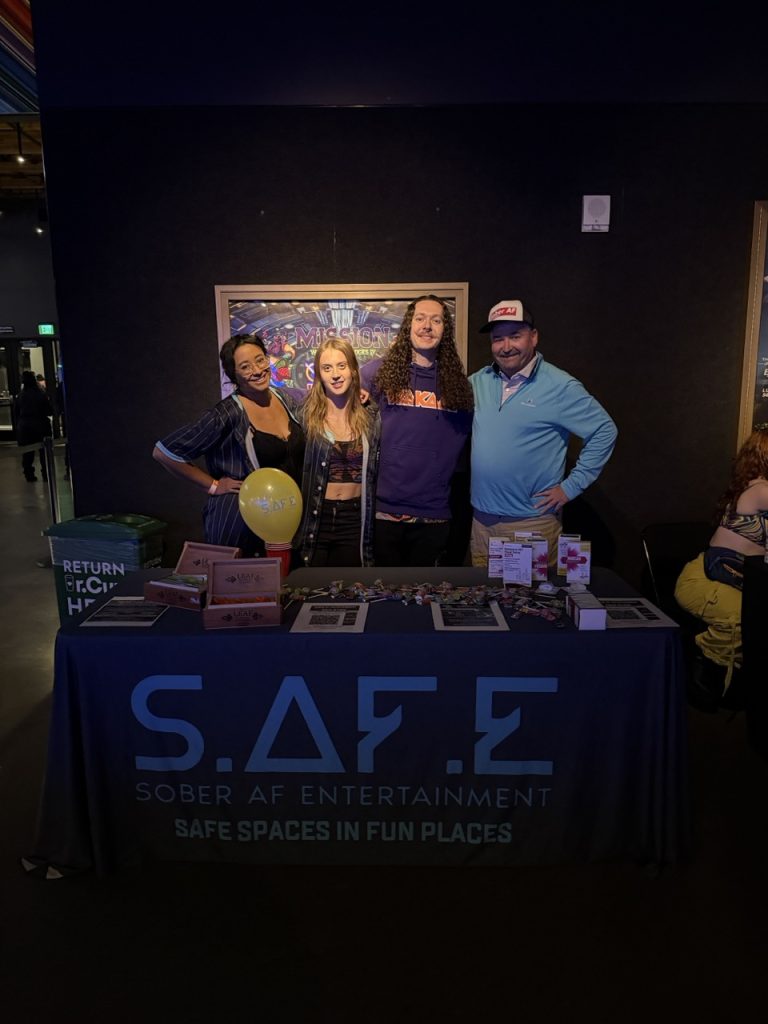 Four people at the S.A.F.E. (Sober AF Entertainment) information table at an indoor event