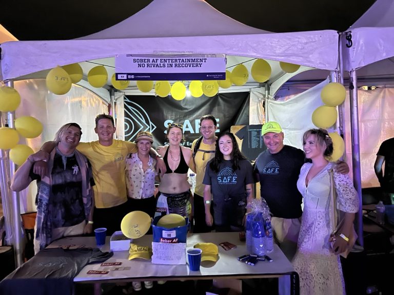 Group of Sober AF Entertainment volunteers and guests at an evening event booth decorated with yellow balloons